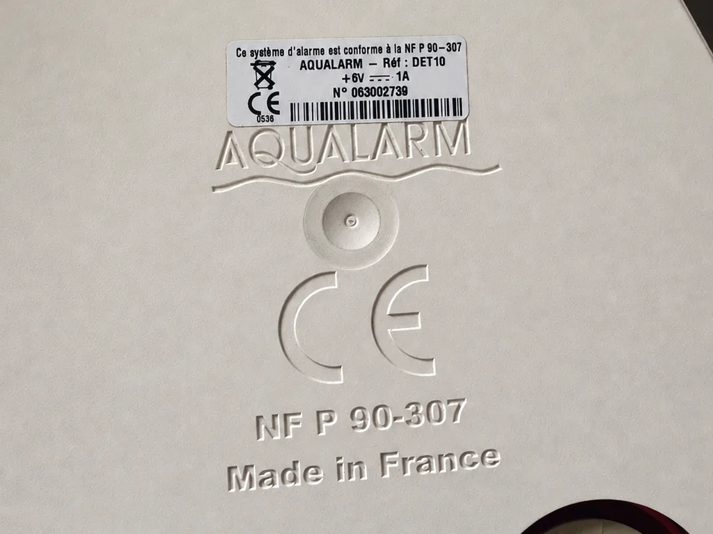 Étiquette de conformité NF P 90-307 sous une alarme de piscine, vérifiée lors d'un contrôle de sécurité